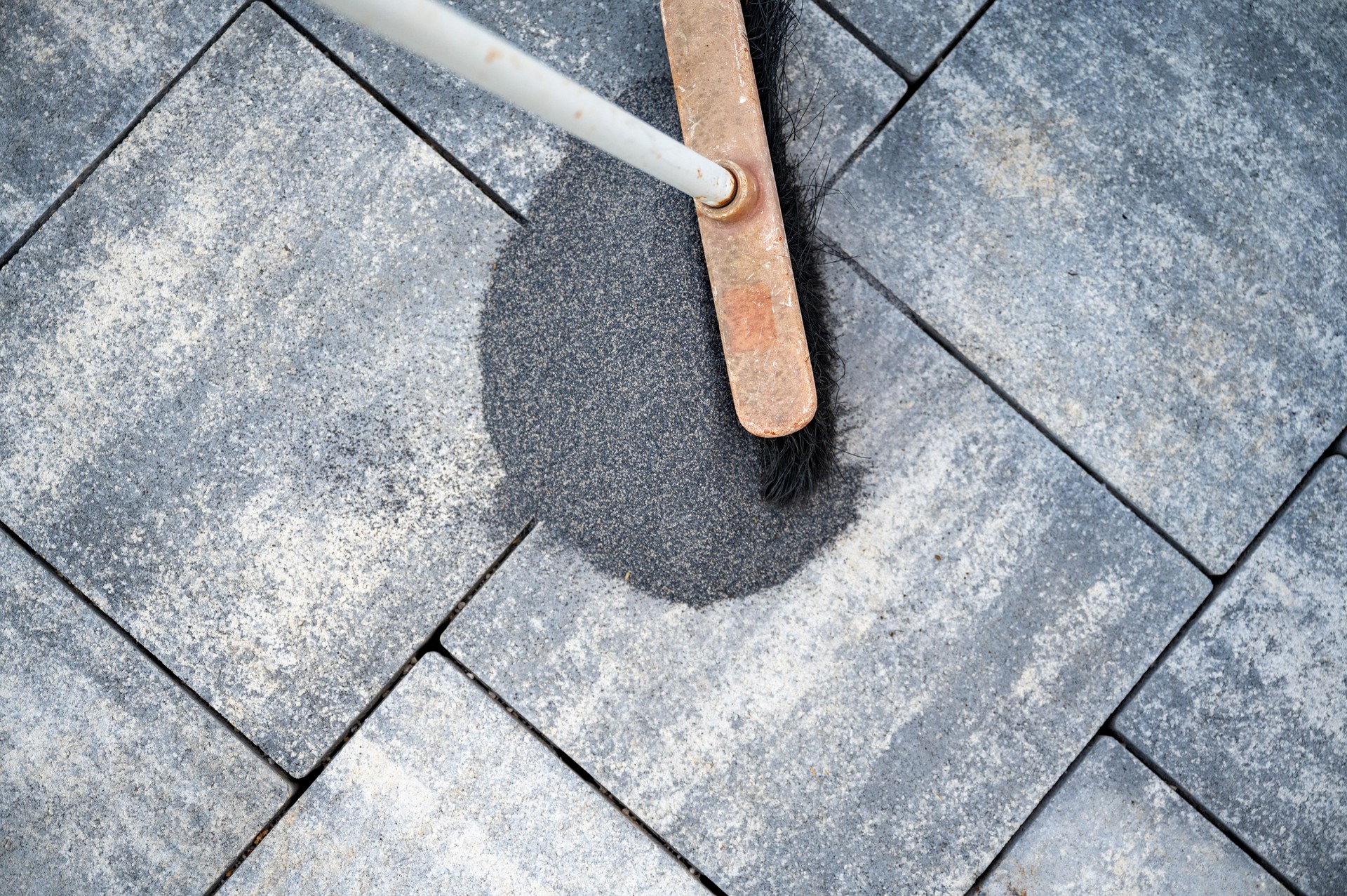 Top view of a broom brushing a tile gap sand in between the gaps of newly paved sidewalk
